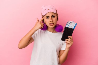 Elinde pasaport ve seyahat biletleri olan beyaz saçlı genç bir kadın pembe arka planda izole edilmiş ve işaret parmağıyla hayal kırıklığına uğramış bir hareket sergiliyor..