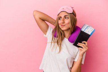 Elinde pasaport ve seyahat biletleri olan beyaz tenli genç bir kadın pembe arka planda izole edilmiş kafasının arkasına dokunuyor, düşünüyor ve bir seçim yapıyor..