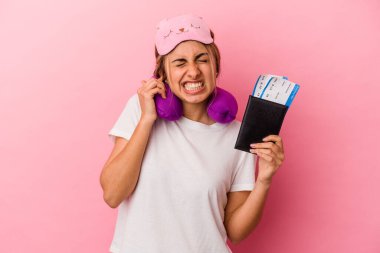 Pasaport ve seyahat biletleri taşıyan beyaz, genç bir kadın. Pembe arka planda izole edilmiş, elleri kulaklarında..
