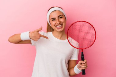 Genç, sarışın, beyaz bir kadın elinde badminton raketi tutuyordu. Pembe arka planda izole edilmiş, elle bir gömlek fotokopisini gösteren, gururlu ve kendinden emin bir kadın.