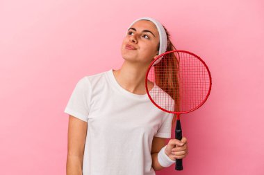 Genç, sarışın, beyaz bir kadın elinde bir badminton raketi tutuyor. Pembe arka planda izole edilmiş. Amaçlarına ve amaçlarına ulaşma hayali kuruyor.