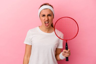 Genç, sarışın, beyaz bir kadın elinde bir badminton raketi tutuyor. Pembe arka planda izole edilmiş. Çok sinirli ve agresif çığlıklar atıyor..