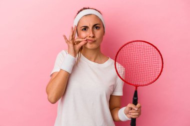 Genç, sarışın, beyaz bir kadın elinde bir badminton raketi tutuyor. Pembe arka planda izole edilmiş ve parmakları dudaklarında bir sır saklıyor..
