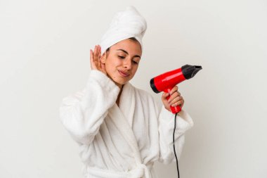 Beyaz tenli, elinde saç kurutma makinesi olan genç bir kadın bir dedikoduyu dinlemeye çalışıyor..