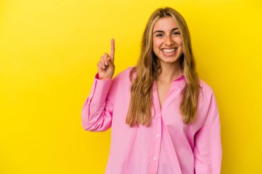 Sarışın, beyaz bir kadın, sarı arka planda izole edilmiş. Bir numarayı parmağıyla gösteriyor..