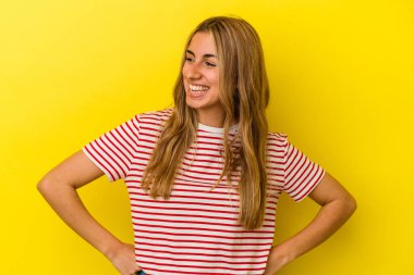 Sarı arka planda izole edilmiş genç sarışın kadın gülüyor ve gözlerini kapıyor, rahatlamış ve mutlu hissediyor..