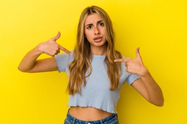 Sarışın, beyaz bir kadın, sarı arka planda izole edilmiş, parmakları aşağıda, olumlu hisler içinde..