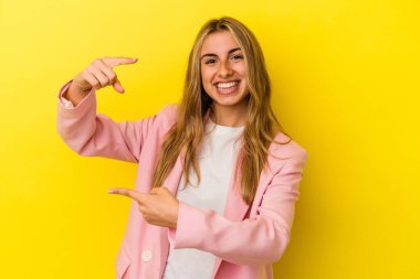 Sarışın, beyaz bir kadın, sarı arka planda izole edilmiş. Elinde küçük bir işaret parmağı var, gülümsüyor ve kendinden emin..