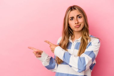Pembe arka planda izole edilmiş genç sarışın beyaz kadın işaret parmağıyla fotokopi alanını işaret ederek şok oldu..