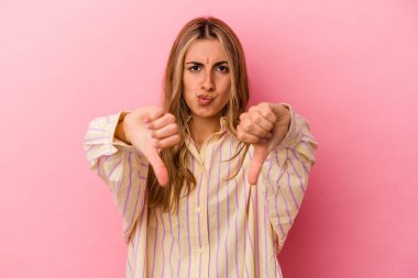 Pembe arka planda izole edilmiş genç sarışın kadın baş parmağını aşağı gösteriyor ve hoşlanmadığını ifade ediyor..