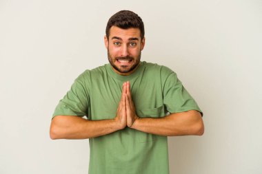 Beyaz arka planda izole edilmiş genç beyaz bir adam el ele tutuşup, ağız kenarında dua ediyor, kendinden emin..