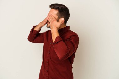 Beyaz arka planda izole edilmiş genç beyaz bir adam elleriyle gözlerini kapatmaktan korkuyor..