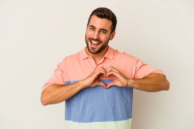 Beyaz arka planda izole edilmiş genç beyaz bir adam gülümsüyor ve elleriyle kalp şekli gösteriyor..
