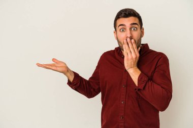 Beyaz arka planda izole edilmiş genç beyaz adam, avuç içi fotokopi alanını elinde tutmaktan etkilenmiş..