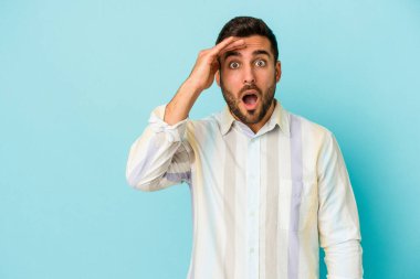 Mavi arka planda izole edilmiş genç beyaz adam yüksek sesle bağırıyor, gözleri açık ve elleri gergin tutuyor..