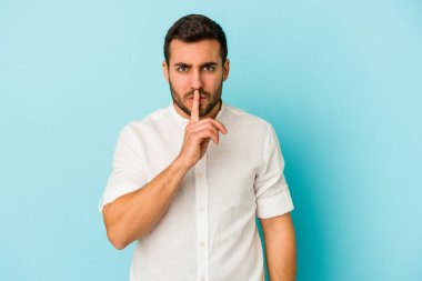 Mavi arka planda izole edilmiş genç beyaz bir adam ya sır saklıyor ya da sessizlik istiyor..