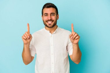 Mavi arka planda izole genç beyaz adam işaret iki ön parmakları boş bir boşluk gösteren.