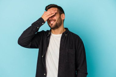 Mavi arka planda izole edilmiş genç beyaz adam ellerini başının üstünde tutarak neşe içinde gülüyor. Mutluluk kavramı.