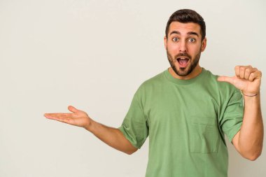 Beyaz arka planda izole edilmiş genç beyaz bir adam bir avuç içinde fotokopi alanı tutuyor, el üstünde tutuyor. Şaşırmış ve mutlu..