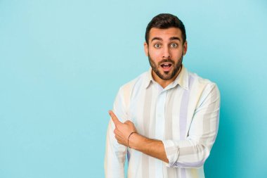Mavi arka planda izole edilmiş genç beyaz adam yan tarafı işaret ediyor.