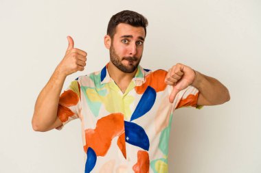 Beyaz arka planda izole edilmiş genç beyaz bir adam baş parmaklarını aşağı ve yukarı kaldırıyor, zor seçim konsepti