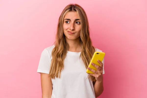 Joven Rubia Caucásica Sosteniendo Teléfono Móvil Amarillo Aislado Confundido Siente —  Fotos de Stock