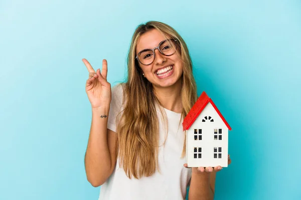 Junge Kaukasische Frau Hält Ein Auf Blauem Hintergrund Isoliertes Hausmodell — Stockfoto