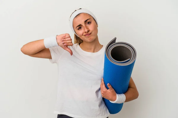 年轻的女运动员拿着一个被白色背景隔离的垫子 表现出不喜欢的姿态 大拇指垂下 不同意的概念 — 图库照片