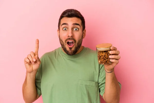 Joven Caucásico Sosteniendo Frasco Almendras Aislado Sobre Fondo Rosa Teniendo —  Fotos de Stock