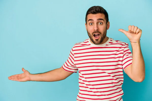 Young Caucasian Man Isolated Blue Background Holds Copy Space Palm — Stock Photo, Image