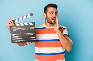 Mavi arka planda el çırpma tahtası tutan genç beyaz bir adam gizli sıcak fren haberini veriyor ve yana bakıyor.