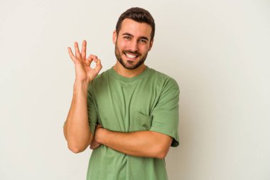 Beyaz arka planda izole edilmiş genç beyaz bir adam bir göz kırptı ve elleriyle iyi bir jest yaptı..