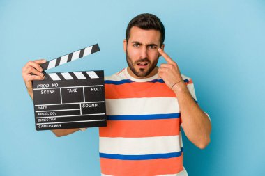 Kafkasyalı genç bir adam mavi arka planda izole edilmiş bir şekilde işaret parmağıyla hayal kırıklığı jesti yapıyor..