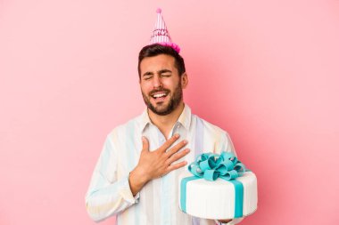 Pembe arka planda yalnız başına doğum gününü kutlayan beyaz bir adam kahkahalar atıyor..