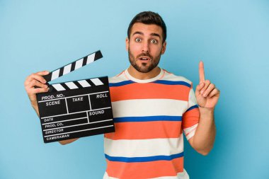 Kafkasyalı genç bir adam mavi arka planda izole edilmiş bir alçıpan tutuyor. Harika bir fikri var, yaratıcılık kavramı..