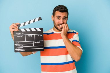 Mavi arka planda izole edilmiş, tırnak yiyen, gergin ve endişeli genç beyaz bir adam..