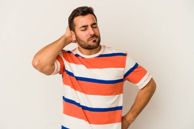 Beyaz arka planda izole edilmiş genç beyaz bir adam yorgun ve uykulu bir şekilde elini başının üstünde tutuyor..