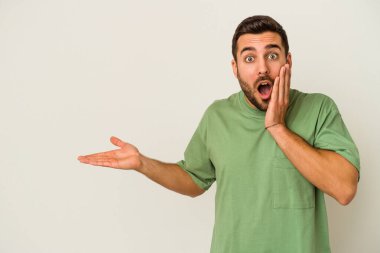 Beyaz arka planda izole edilmiş genç beyaz adam, avuç içi fotokopi alanını elinde tutmaktan etkilenmiş..