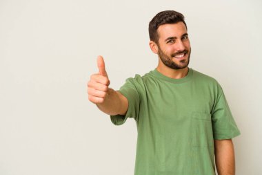 Beyaz arka planda izole edilmiş genç beyaz adam gülümsüyor ve başparmağını kaldırıyor.