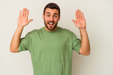 Beyaz arka planda izole genç beyaz adam hoş bir sürpriz alıyor, heyecanlı ve el kaldırıyor..
