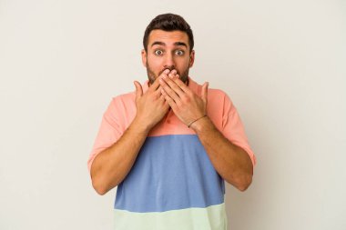 Beyaz arka planda izole edilmiş genç beyaz adam elleriyle ağzını kapatırken şok oldu..