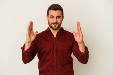 Beyaz arka planda izole edilmiş genç beyaz bir adam işaret parmaklarıyla küçük bir şey tutuyor, gülümsüyor ve kendinden emin..