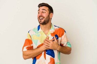 Beyaz arka planda soyutlanmış beyaz tenli genç bir adam gülüyor, elini yüreğine koyuyor, mutluluk kavramını koruyor..