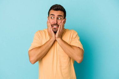 Kafkasyalı genç adam mavi arka planda izole edilmiş korkmuş ve korkmuş..