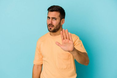 Mavi arka planda izole genç beyaz adam yakın bir tehlike nedeniyle şoka uğruyor