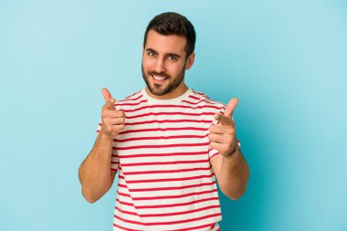 Mavi arka planda izole edilmiş genç beyaz adam parmaklarıyla ön tarafı işaret ediyor..