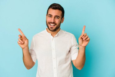 Mavi arka planda izole edilmiş genç beyaz adam farklı kopya alanlarını gösteriyor, birini seçiyor, parmaklarıyla gösteriyor.