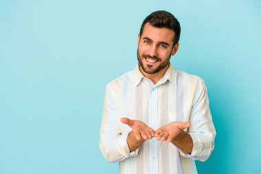 Kafkasyalı genç adam mavi arka planda izole edilmiş dudaklar kıvrılıyor ve hava öpücüğü göndermek için avuç içleri tutuyor..