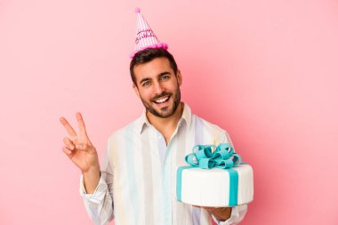 Doğumgününü kutlayan beyaz bir adam pembe arka planda izole edilmiş neşeli ve kaygısız parmaklarıyla barış sembolü gösteriyor..
