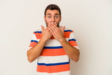 Beyaz arka planda izole edilmiş genç beyaz adam elleriyle ağzını kapatırken şok oldu..
